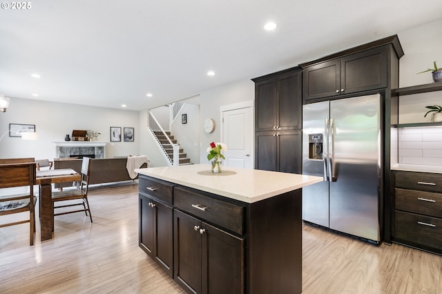 kitchen featuring stainless steel refrigerator with ice dispenser, light wood-style flooring, a fireplace, light countertops, and recessed lighting