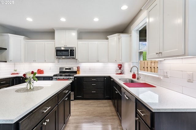 kitchen featuring stainless steel appliances, a sink, white cabinets, light wood finished floors, and recessed lighting