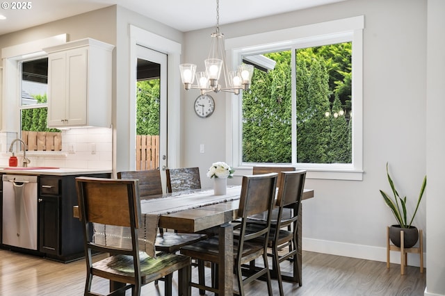 dining room with healthy amount of natural light, a chandelier, baseboards, and light wood-type flooring