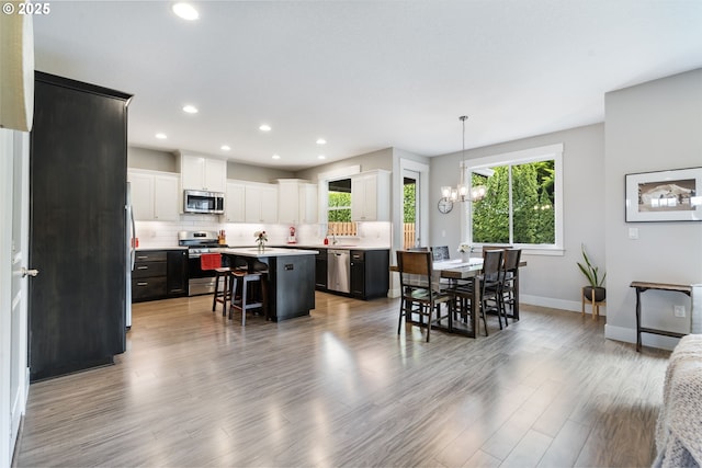 kitchen featuring stainless steel appliances, a kitchen bar, baseboards, decorative backsplash, and a kitchen island with sink