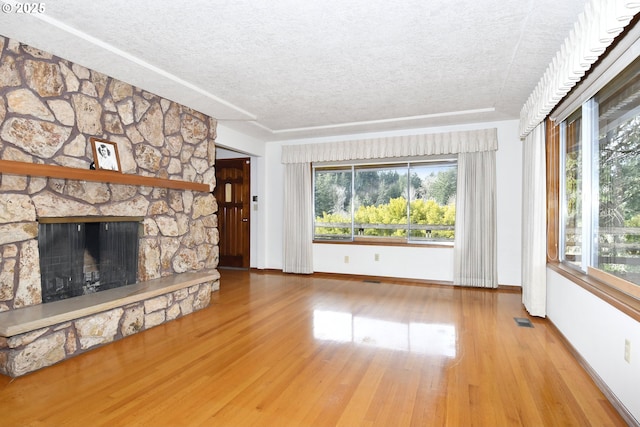 unfurnished living room featuring wood-type flooring, a stone fireplace, plenty of natural light, and a textured ceiling