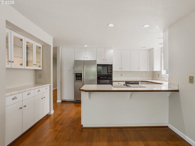 15917 NE Union Rd Unit 103, Ridgefield, WA 98642 - kitchen featuring black appliances, a peninsula, dark wood-style flooring, white cabinets, and glass insert cabinets