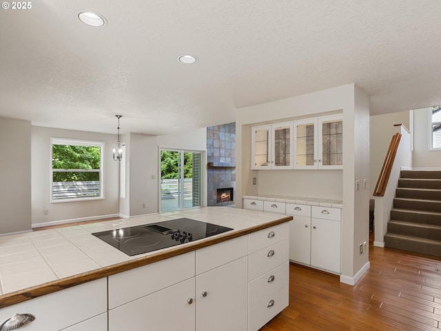 15917 NE Union Rd Unit 103, Ridgefield, WA 98642 - kitchen featuring black electric stovetop, a tile fireplace, wood finished floors, glass insert cabinets, and white cabinetry
