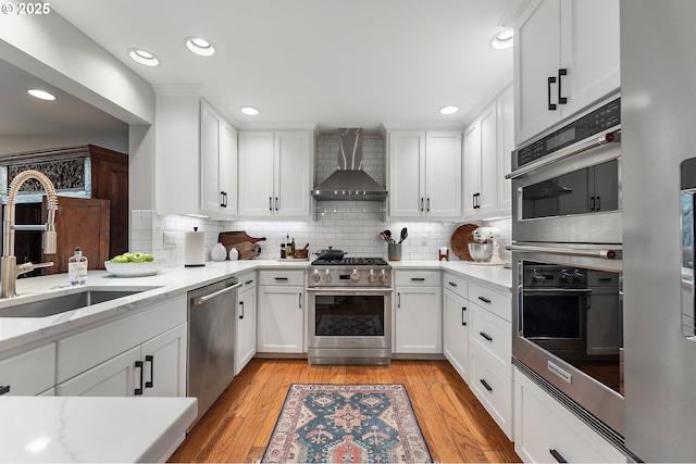 kitchen featuring a sink, stainless steel appliances, white cabinets, light wood-style floors, and wall chimney exhaust hood