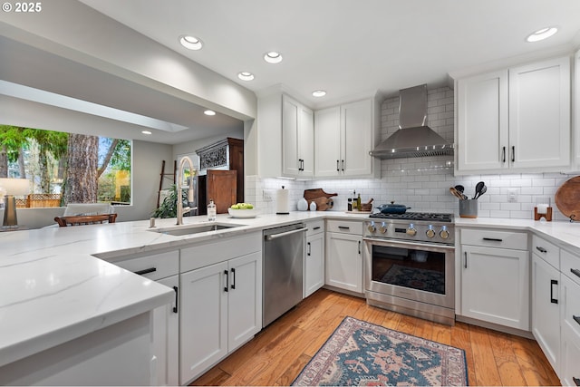 kitchen featuring a sink, wall chimney range hood, light wood-style floors, and stainless steel appliances