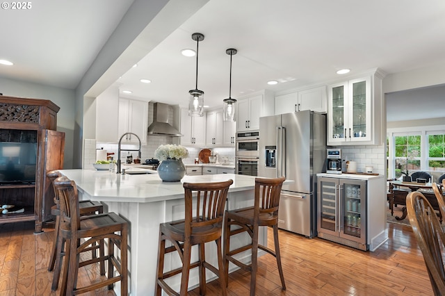 kitchen with a kitchen bar, beverage cooler, wall chimney range hood, stainless steel appliances, and light countertops