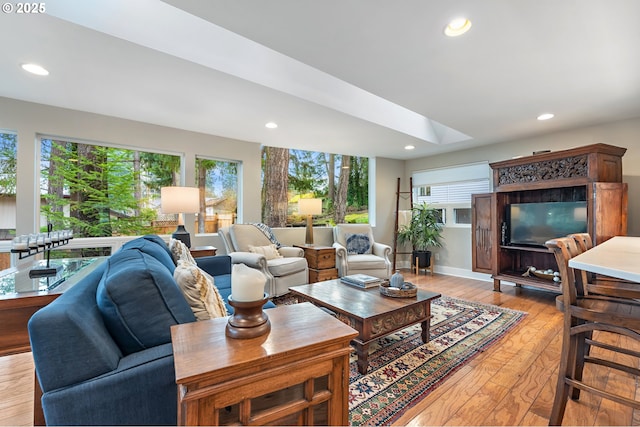 living room featuring a skylight, recessed lighting, light wood-style floors, and baseboards