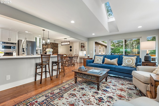 living area featuring a skylight, recessed lighting, baseboards, and light wood finished floors