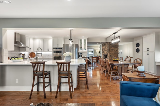 kitchen featuring tasteful backsplash, light countertops, appliances with stainless steel finishes, wall chimney exhaust hood, and a sink