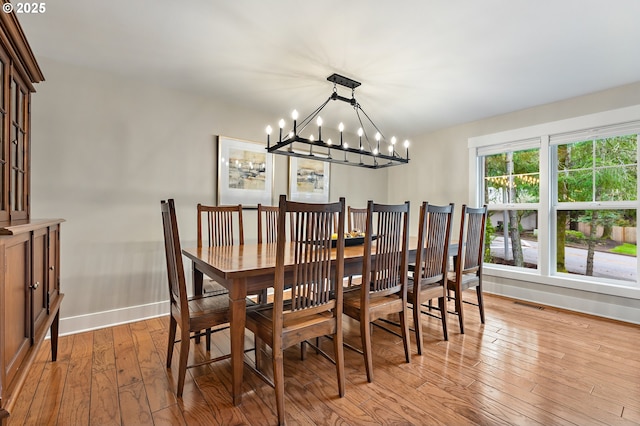 dining space featuring light wood-style flooring, a notable chandelier, visible vents, and baseboards