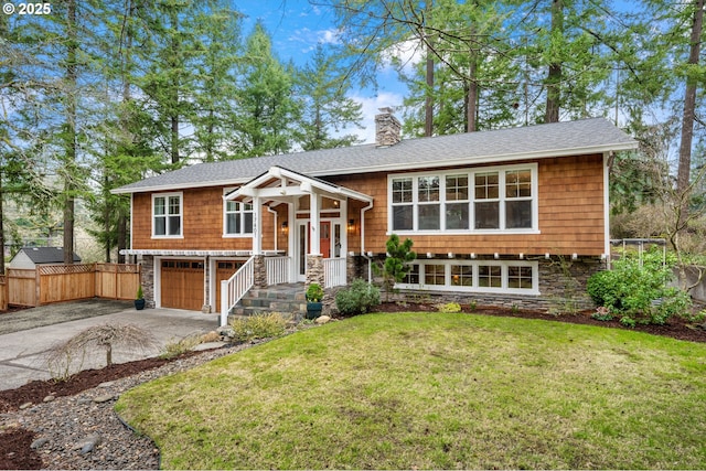 bi-level home with stone siding, driveway, a chimney, and fence