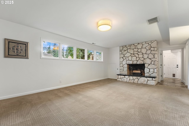 unfurnished living room with visible vents, baseboards, a stone fireplace, and carpet flooring