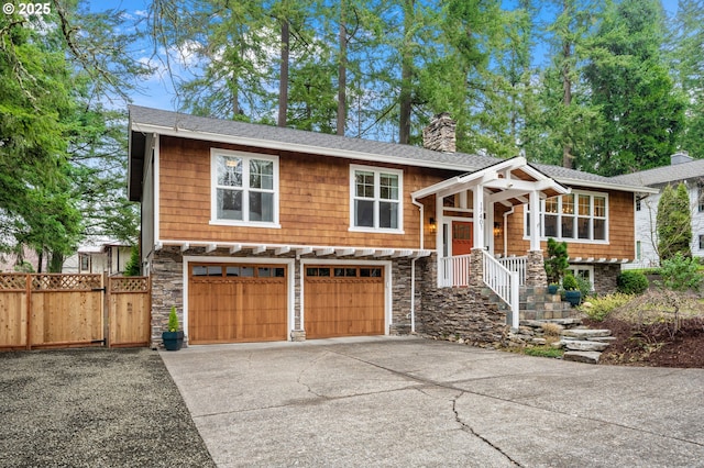 raised ranch with fence, driveway, a chimney, a garage, and stone siding