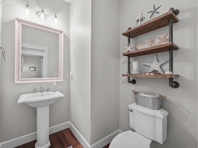 half bathroom with toilet, wood finished floors, and baseboards