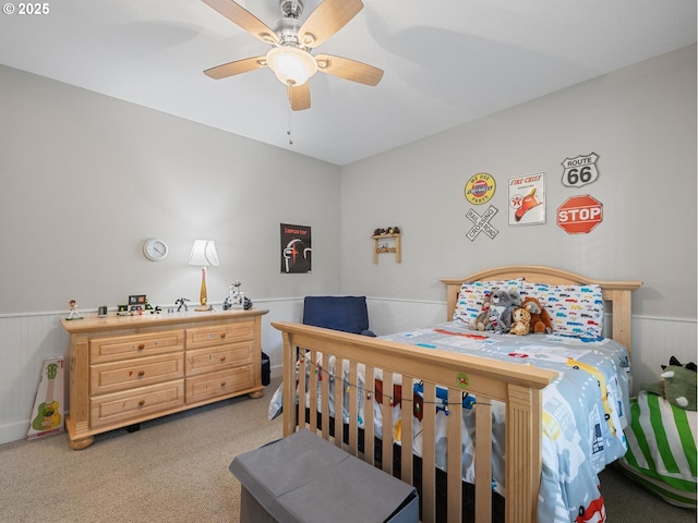 bedroom with light carpet, wainscoting, and ceiling fan