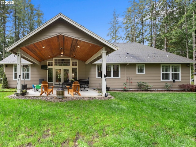 rear view of house featuring a patio area, a lawn, roof with shingles, and an outdoor fire pit