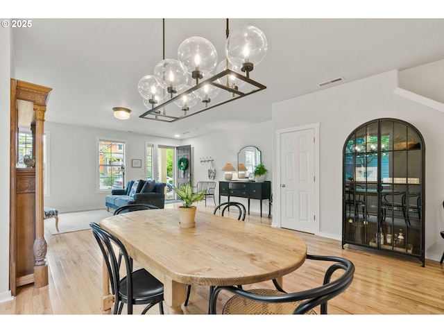 dining room featuring visible vents, light wood-style floors, baseboards, and a notable chandelier