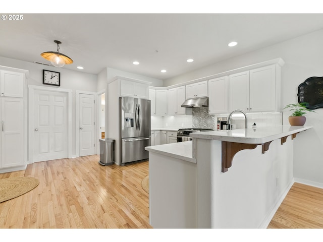 kitchen featuring appliances with stainless steel finishes, white cabinets, under cabinet range hood, and a peninsula