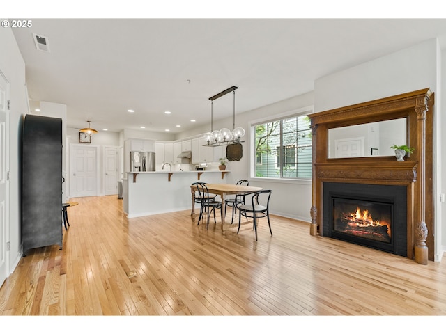 dining space with visible vents, baseboards, a glass covered fireplace, light wood-style floors, and recessed lighting