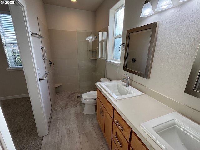 bathroom with toilet, vanity, tiled shower, and a healthy amount of sunlight