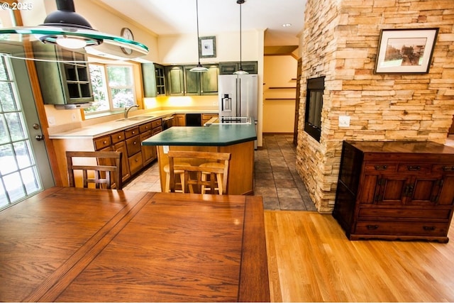kitchen featuring green cabinets, a sink, light wood-style floors, wall oven, and hanging light fixtures