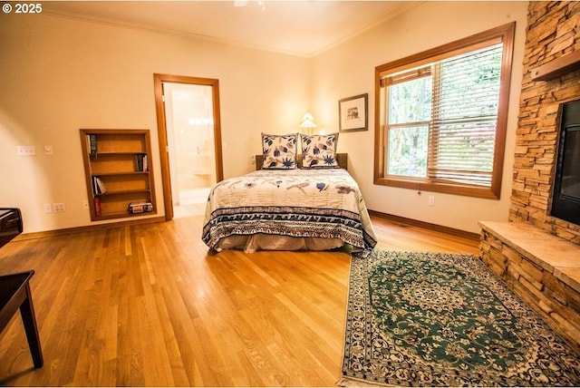 bedroom with wood finished floors, ornamental molding, ensuite bathroom, and baseboards