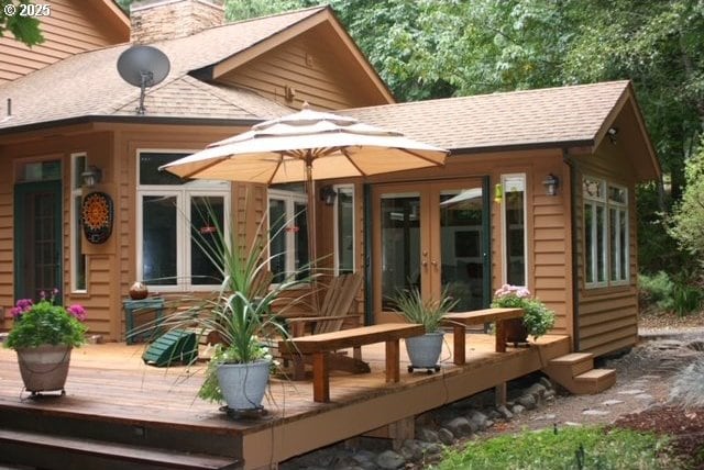 rear view of property with french doors, a deck, roof with shingles, and a chimney