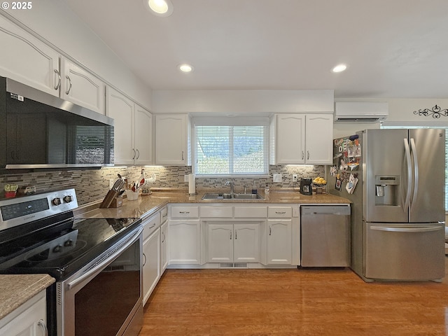 kitchen with light wood-style flooring, a sink, white cabinetry, a wall unit AC, and stainless steel appliances