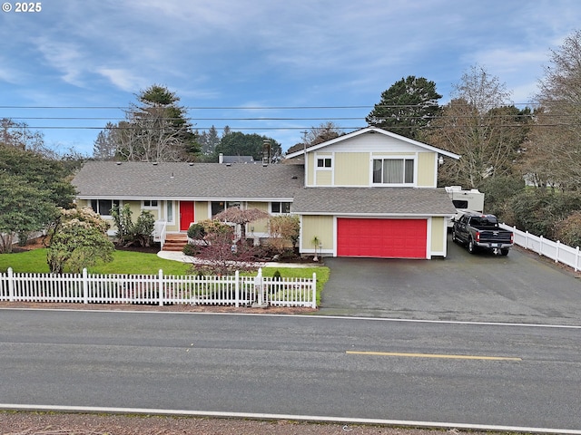 tri-level home featuring a fenced front yard, an attached garage, driveway, and roof with shingles