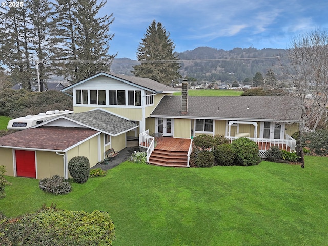 back of property with a lawn, a deck with mountain view, and a shingled roof