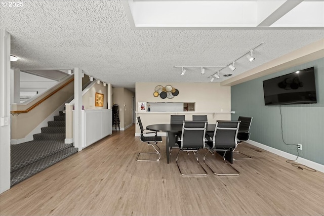 dining space featuring a textured ceiling, stairs, baseboards, and wood finished floors