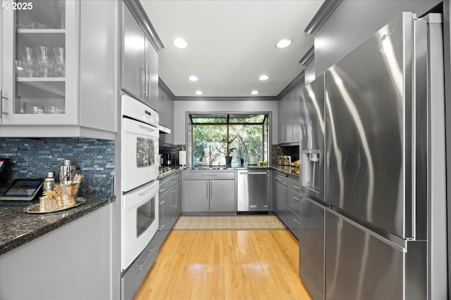 kitchen with light wood-style flooring, gray cabinets, ornamental molding, stainless steel appliances, and tasteful backsplash