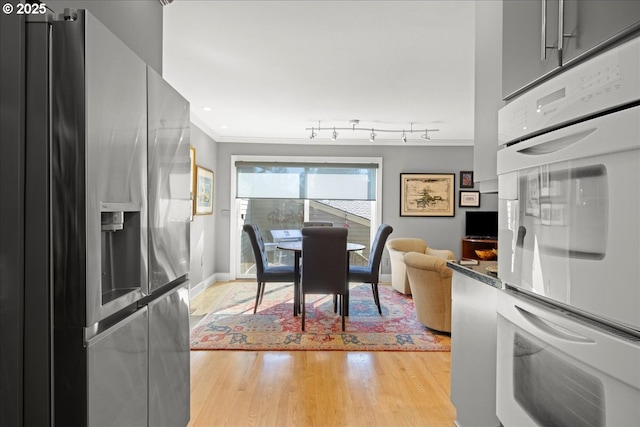 dining room featuring rail lighting, baseboards, crown molding, and light wood-style floors