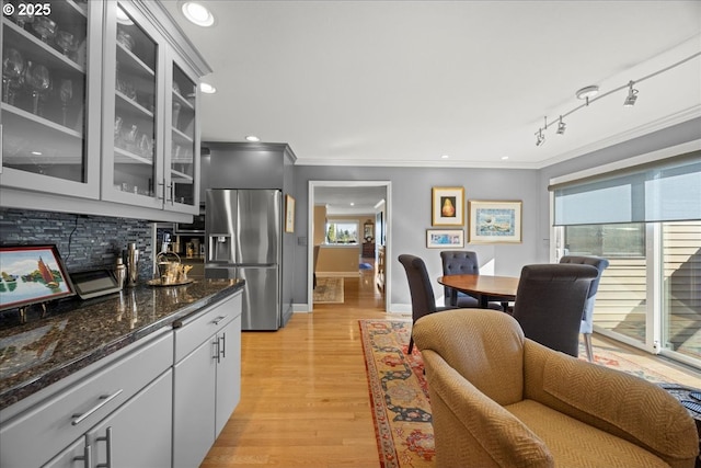 kitchen with backsplash, stainless steel fridge with ice dispenser, light wood finished floors, crown molding, and glass insert cabinets