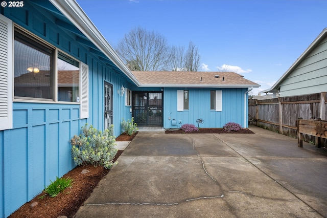 exterior space with a patio, fence, board and batten siding, and a shingled roof