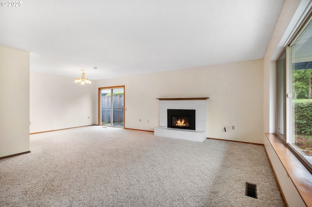 unfurnished living room featuring visible vents, a brick fireplace, baseboards, a chandelier, and carpet floors