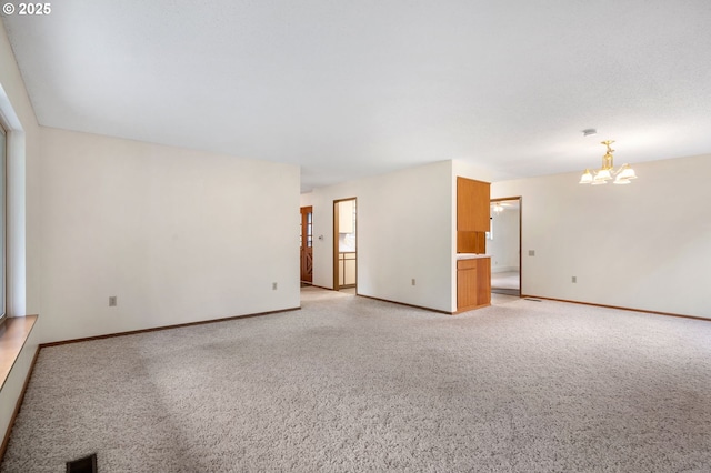 spare room with an inviting chandelier, light colored carpet, visible vents, and baseboards