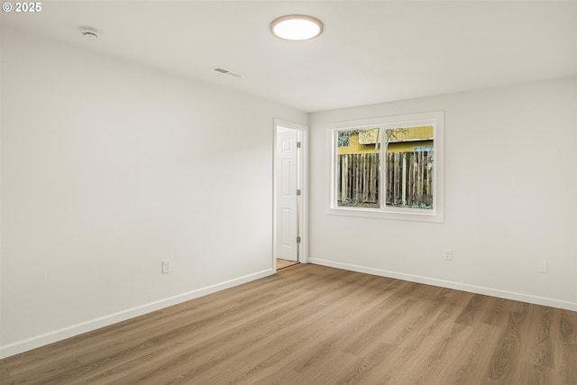 empty room featuring light wood-style floors, visible vents, and baseboards