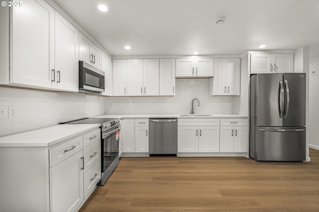 kitchen featuring appliances with stainless steel finishes, white cabinets, a sink, and wood finished floors