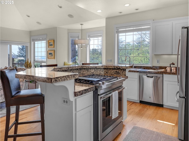 kitchen with a kitchen bar, a sink, light wood finished floors, stainless steel appliances, and white cabinetry