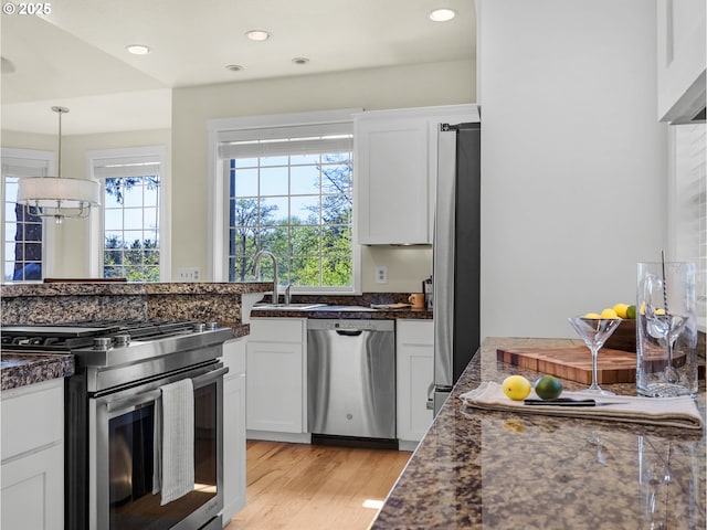 kitchen with white cabinets, a sink, light wood finished floors, appliances with stainless steel finishes, and decorative light fixtures
