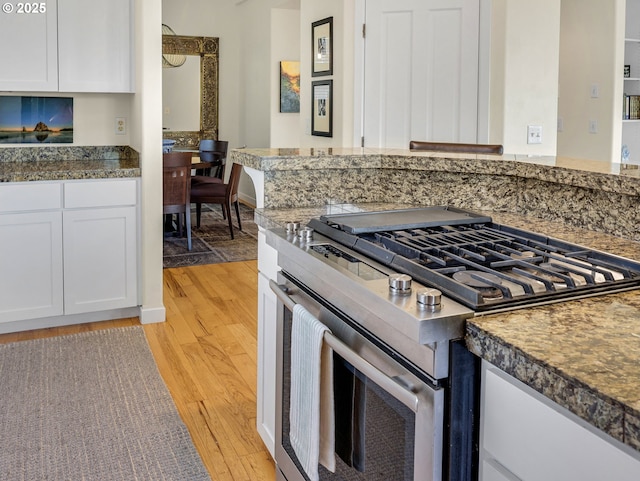 kitchen with tile counters, light wood-style flooring, stainless steel gas stove, and white cabinetry