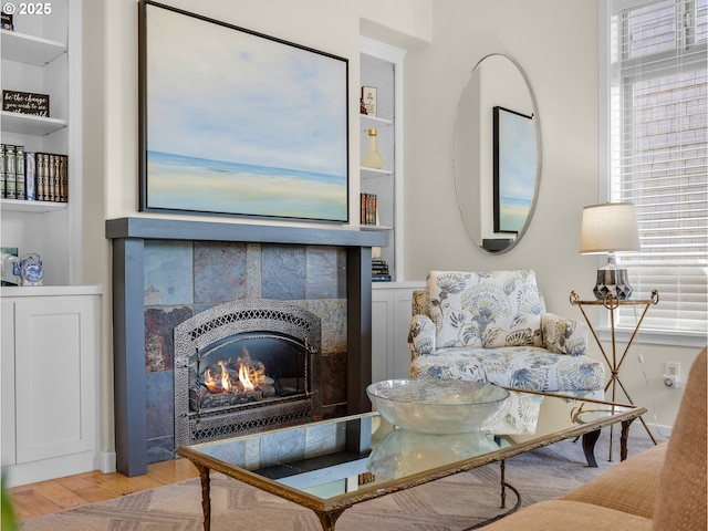 sitting room featuring a tiled fireplace, wood finished floors, and built in shelves