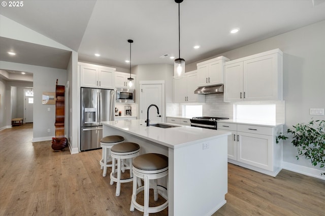 1332 SE 14th Ave, Canby, OR 97013 - kitchen with stainless steel appliances, a sink, under cabinet range hood, decorative backsplash, and light wood-type flooring