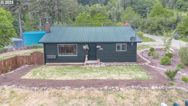 view of front of house featuring metal roof, a chimney, a gate, and a forest view