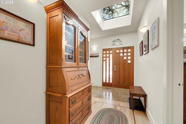 entrance foyer with a skylight, light wood-type flooring, and baseboards