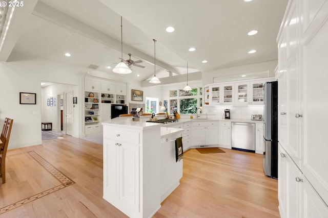 kitchen featuring light wood finished floors, vaulted ceiling with beams, appliances with stainless steel finishes, white cabinets, and a sink