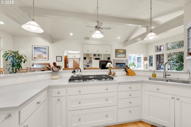 kitchen with stainless steel gas cooktop, light countertops, lofted ceiling with beams, and a sink