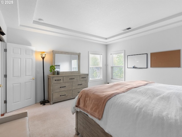 bedroom featuring a tray ceiling, visible vents, and light carpet