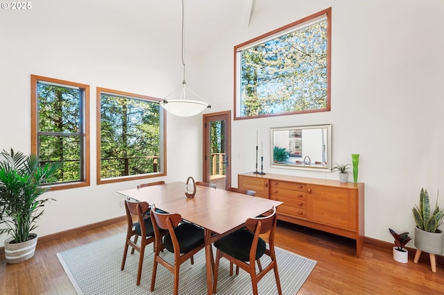 dining area with baseboards, light wood-style floors, and a high ceiling
